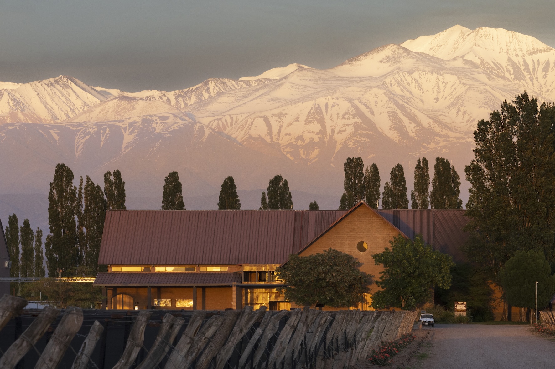 Susana Balbo Winery in Agrelo, Luján de Cuyo, with its buildings surrounded by trees and the snow-capped Andes Mountains in the background.