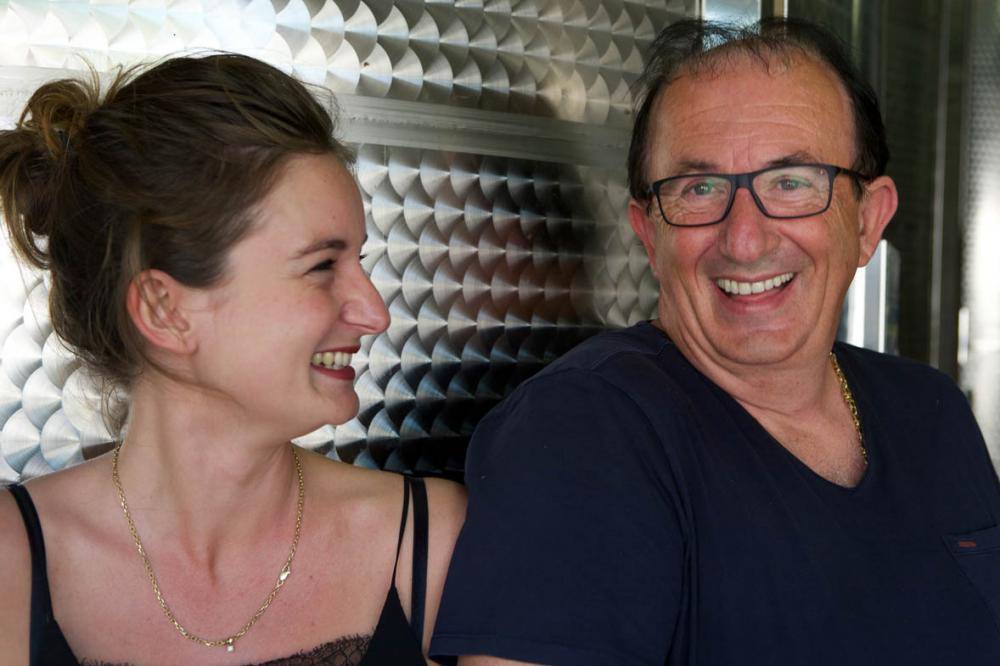 A woman and a man laughing together in front of a stainless steel wine tank.