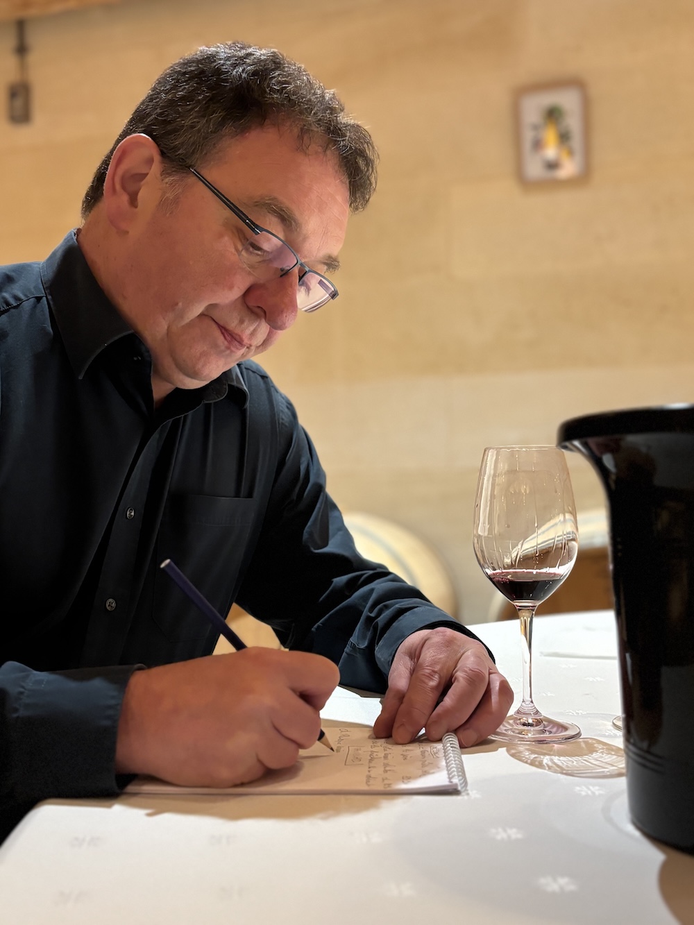 Writing tasting notes on a glass of Bordeaux 2025 Primeurs red wine