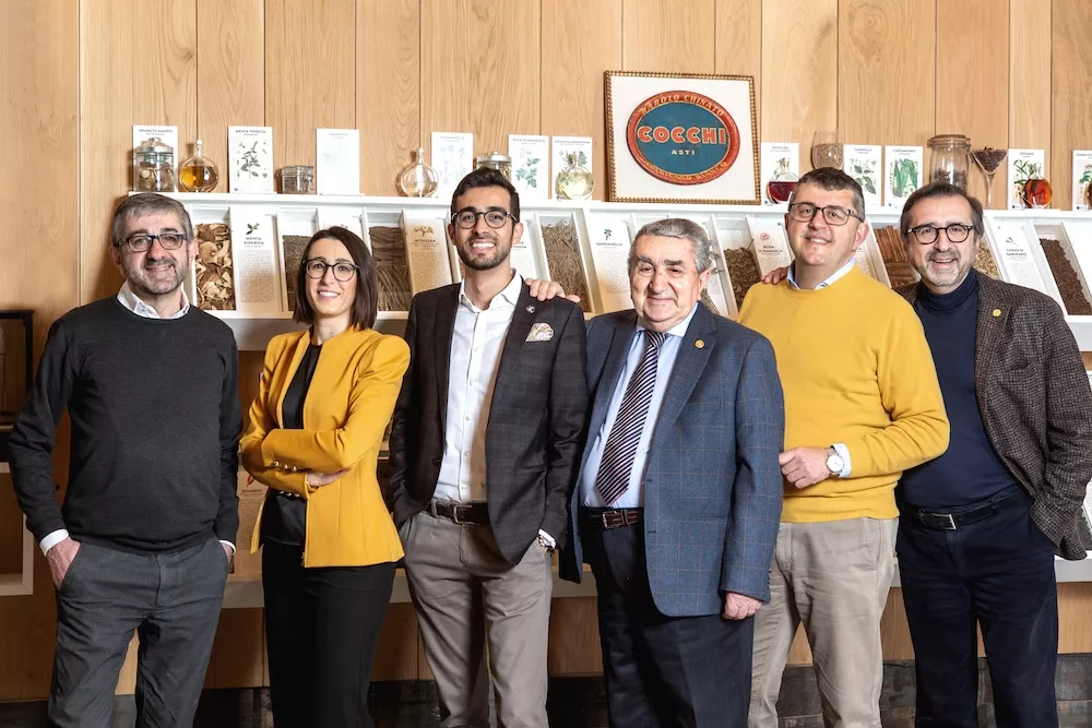 The Bava family, six people posing in front of shelves of bottles beneath the Cocchi sign