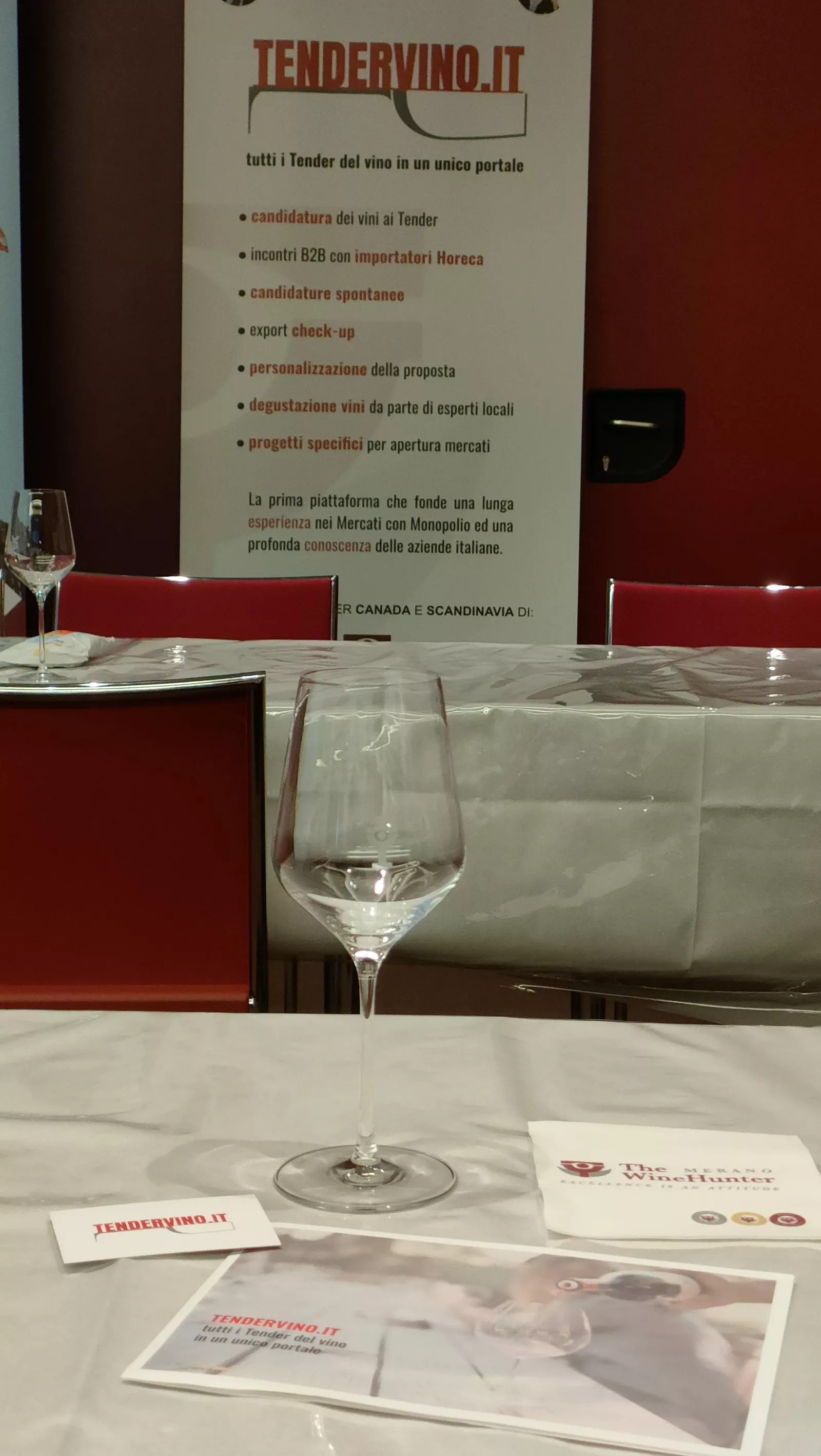 Tendervino banner behind a table laid with a white cloth, a wine glass and brochures